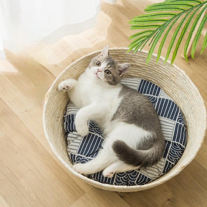 A beautiful black and white cat is lounging in a straw matted cat bed.